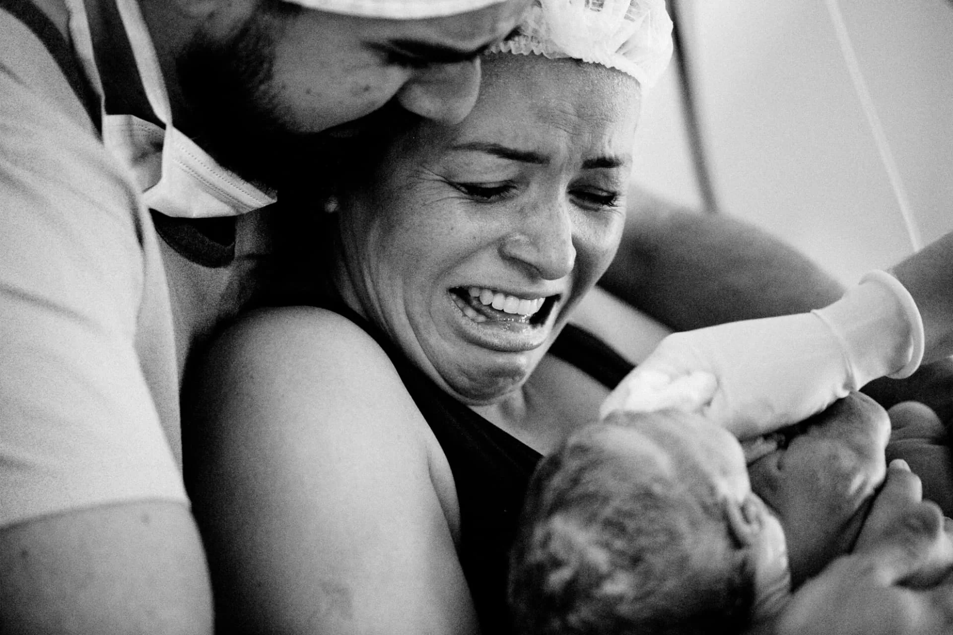 Mãe emocionada recebendo o bebê no colo logo após o nascimento, com o pai ao lado
